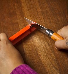 a person holding a pair of scissors on top of a wooden table with an orange handle