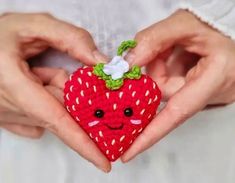 a person holding a small red strawberry with a smile on it's face in their hands