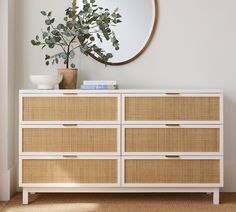 a white dresser with wicker drawers and a round mirror above it on the wall