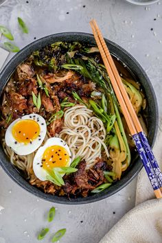 a bowl filled with noodles, meat and vegetables next to chopsticks