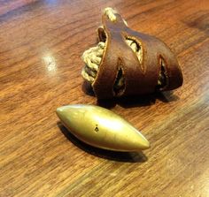 a small brass object sitting on top of a wooden table next to a leather bracelet