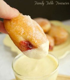 a hand holding a donut over a glass filled with pudding