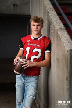 a young man is holding a football and posing for a photo on the sidelines