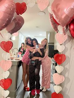 three women taking a selfie in front of balloons and heart - shaped garlands