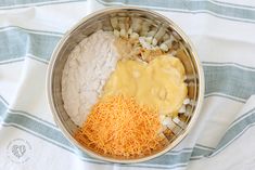 a metal bowl filled with cheese, onions and grated cheese on a blue and white towel