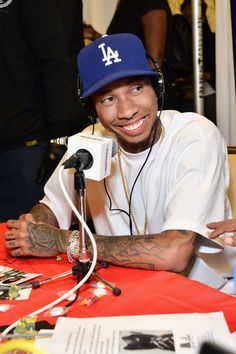 a man sitting at a table with a microphone in front of him and wearing a dodgers hat