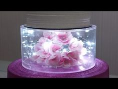 pink flowers are in a clear container with lights