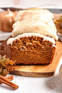 a loaf of pumpkin spice bread with frosting on a cutting board next to some cinnamon sticks