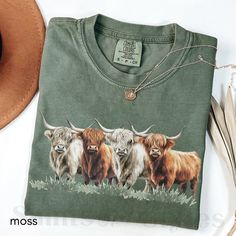 a green shirt with three long horn bulls on it and a hat next to it