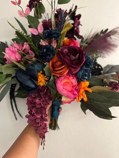 a bouquet of flowers is being held by someone's hand in front of a white wall