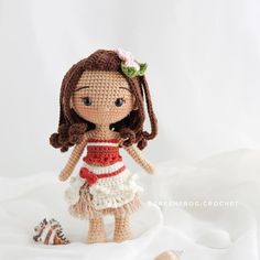 a crocheted doll is standing next to a seashell on a white sheet