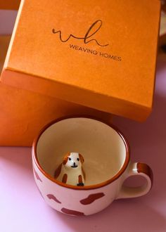 a dog figurine sitting in a coffee cup next to an orange gift box