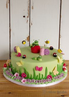 a green cake decorated with bugs and flowers on top of a wooden table in front of a white painted wall