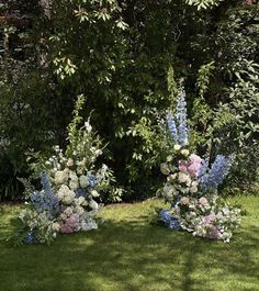 three tall vases with flowers in the middle of grass and trees behind them, all on either side of each other