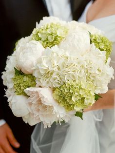 a bride and groom holding a bouquet of white hydrangeas on their wedding day