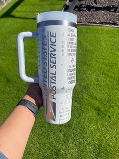 a person holding up a travel mug in their hand on the grass with an artificial park behind them