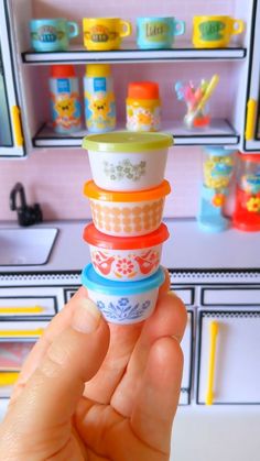 there is a hand holding a stack of plastic cups in front of a toy shelf