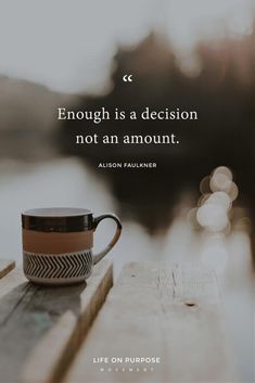 a coffee cup sitting on top of a wooden table next to the water with a quote about enough is a decision not an amount