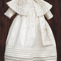 a white dress with embroidered details on the collar and sleeves, is displayed against a wooden background