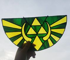 a hand holding up a stained glass kite with the symbol of legend of zelda on it