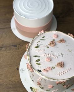 two cakes decorated with pink flowers and leaves on top of each other, sitting on plates