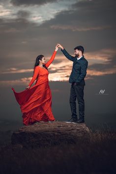 a man and woman standing on top of a rock holding each other's hands