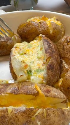 baked potatoes with cheese and melted cheese on them in a white bowl next to a fork