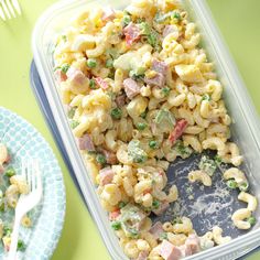 a plastic container filled with macaroni salad next to a blue and white plate