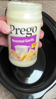 a hand holding a jar of prego toasted garlic on top of a black plate