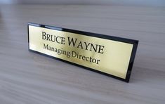 a gold and black sign that says bruce wayne managing director on the side of a wooden table