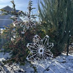 a metal snowflake sitting next to a tree in the snow