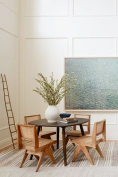 a dining room table with chairs and a vase on it in front of a painting