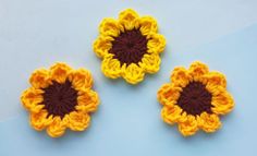 three crocheted sunflowers sitting next to each other on a blue surface