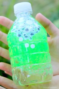 a person holding a plastic bottle with bubbles on it in their hand and the top half of the bottle is green