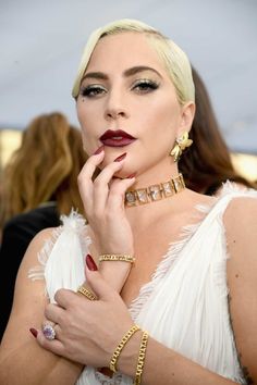 lady in white dress with red lipstick and gold bracelets posing for the camera at an event