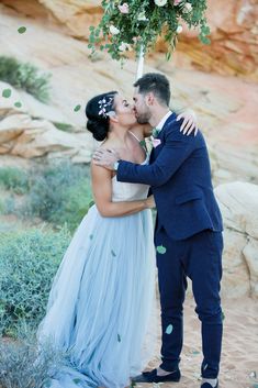 a bride and groom kissing under an arch with greenery in the background at their desert wedding