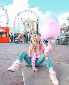 a woman sitting on the ground with a large cotton candy ball in her hand,