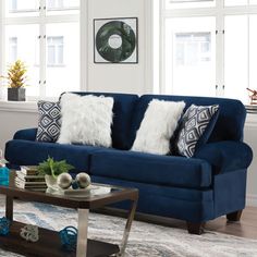 a living room with blue couches and pillows on the table in front of two windows