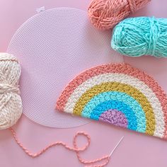 crochet and yarns laid out on a pink surface with a rainbow motif