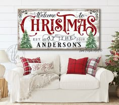 a christmas sign on the wall above a couch in a living room with red and white pillows