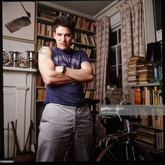 a man standing in front of a bookshelf with his arms crossed and looking at the camera