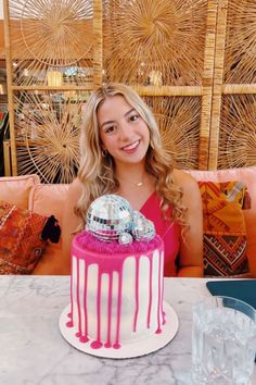 a woman sitting at a table with a pink and white cake in front of her