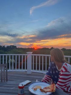 a woman sitting on a deck eating pizza at sunset