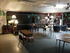 an empty classroom with desks, chairs and lights hanging from the ceiling in front of blackboard