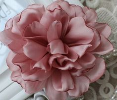 a large pink flower sitting on top of a lace covered table cloth next to a book