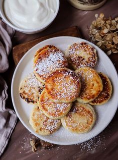 a white plate topped with pancakes covered in powdered sugar next to bowls of yogurt