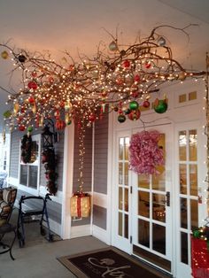 the front porch is decorated for christmas with lights and ornaments hanging from the tree branch