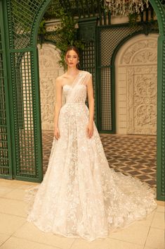 a woman standing in front of a green archway wearing a white dress with flowers on it