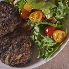 two hamburger patties with tomatoes and lettuce on a plate next to a salad