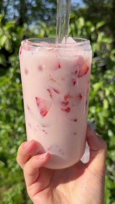 a person holding up a drink with strawberries on it in front of some bushes